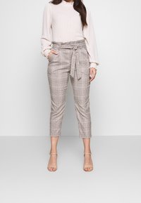 Rutiga beskurna byxor i beige och brunt, med midjebälte och sidofickor, tillsammans med en ljus, strukturerad långärmad topp.