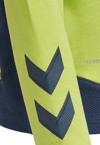 Högsynlig långärmad skjorta med en klar gul kropp, texturerade marinblå accenter och mörka chevronmönster på ärmarna.