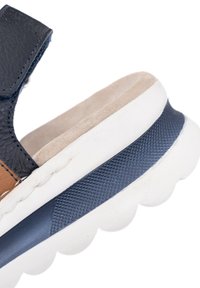 Close-up of navy and brown leather sandal with cushioned beige insole and white sole featuring blue textured grip strip.