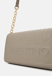 Valentino taška z béžové kůže s pozlacenými hroty a embosovaným logem. Řetězový popruh dodává moderní nádech elegantnímu designu.