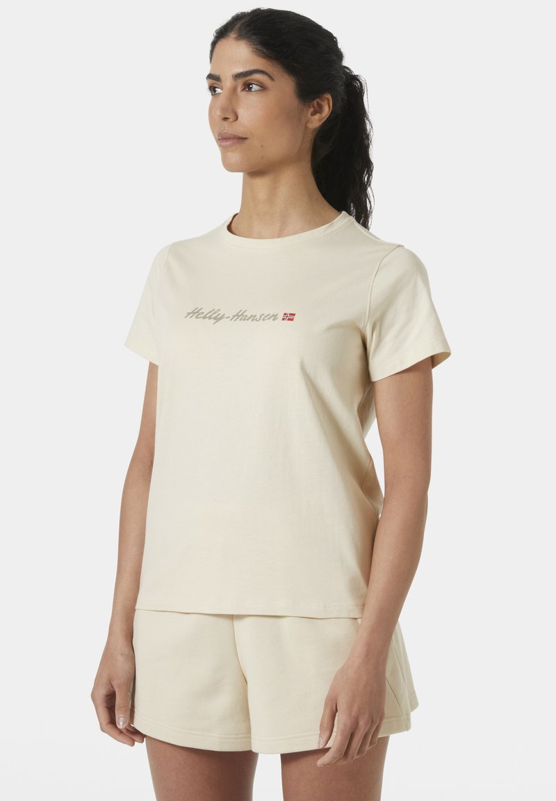 Béžové bavlněné tričko s krátkými rukávy a kulatým výstřihem, s logem "Helly Hansen" v světle hnědé barvě. V kombinaci s odpovídajícími béžovými šortkami.