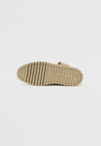Semelle d'une chaussure en beige clair avec un motif texturé, présentant des rainures profondes et un bord arrondi. Logo embossé au bas.