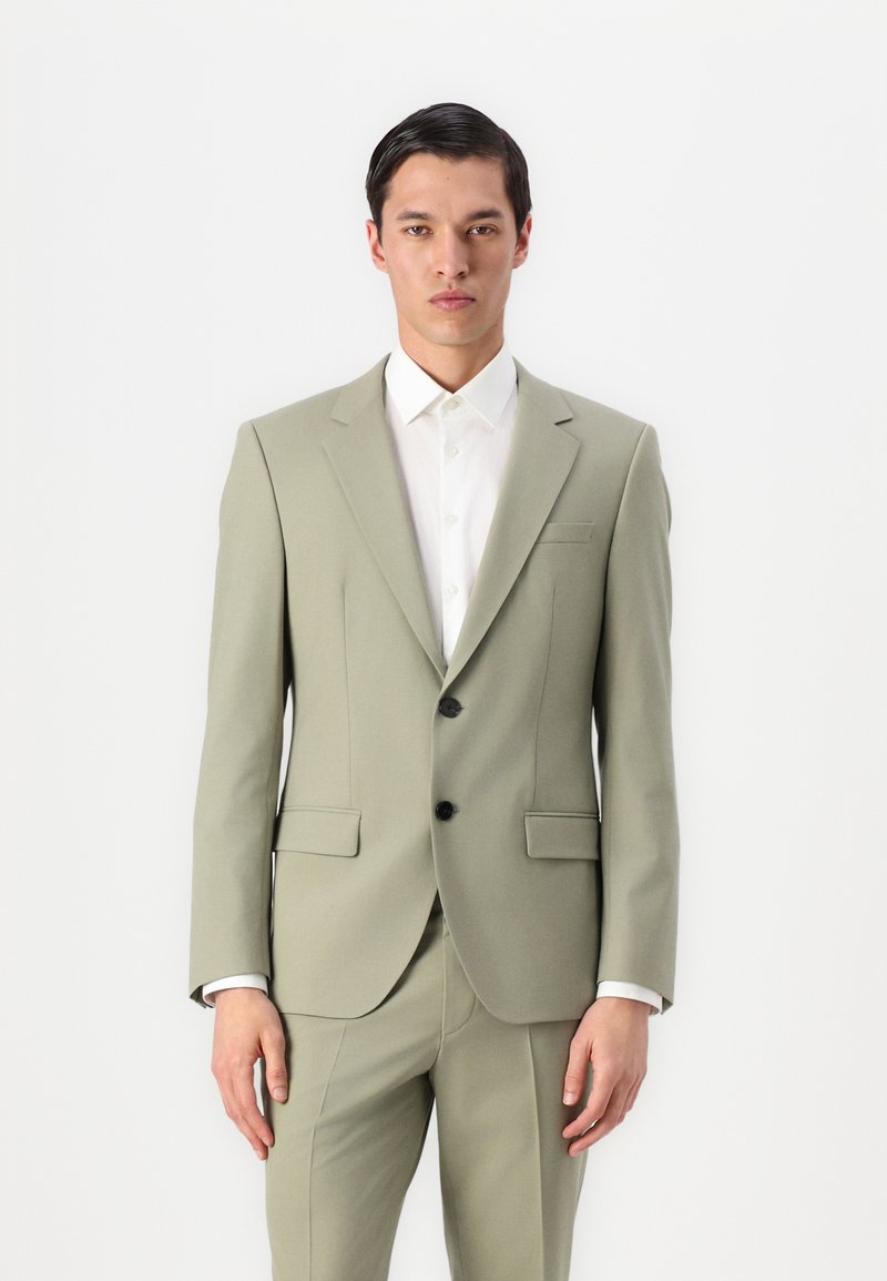 Traje verde claro a medida con chaqueta de un solo botón, botones negros, solapas con muesca y pantalones ajustados a juego. Camisa blanca por debajo.