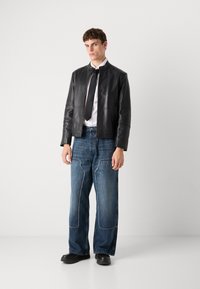 Črna usnjena jakna z visokim ovratnikom, bela srajca, črna kravata in široki modri jeans z kontrastnim šivanjem. Črne čevlje.
