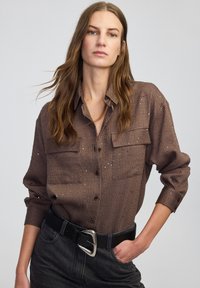 Bruine gestreepte button-up shirt met twee borstzakken en een gestructureerde stof. Draag het met een zwarte riem met een grote zilveren gesp.