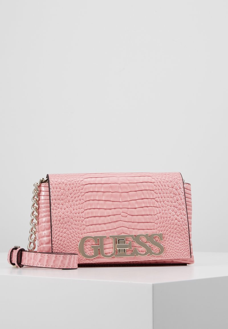 Rosa faux læder crossbody taske med krokodilletekstur, metallisk guld "GUESS" logo, kædestrop og en struktureret rektangulær form.