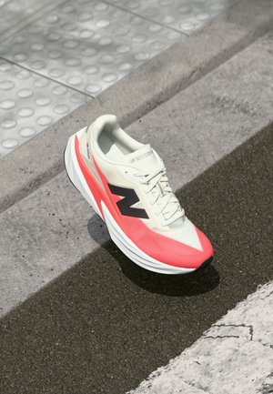 Chaussure de course New Balance blanche et rose sur l'asphalte près d'un bord en béton et d'un trottoir texturé.