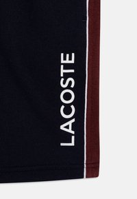 Tengerészkék és bordó pamut keverék rövidnadrág, fehér "LACOSTE" logóval, oldalsó panelek kiemelésével és sima textúrával.