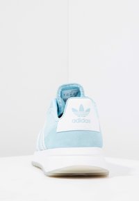 Light blue suede athletic shoe with mesh details, white stripes, and a white heel cap featuring the Adidas logo. White sole.