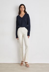 Marineblauw V-hals trui, relaxed fit, met lange mouwen. Crème op maat gemaakte broek met zij-splitten, gecombineerd met beige enkellaarsjes met enkelband.