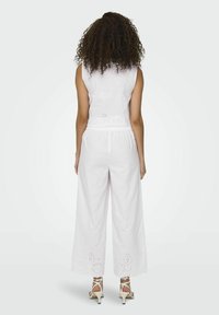 Witte mouwloze top met geperforeerde details aan de zoom, gecombineerd met wijdlopende witte broek met geborduurde bloemenuitsparingen op de enkels.