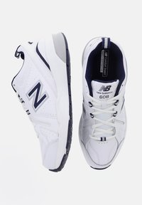 Pair of white New Balance 608 sneakers with navy details, visible logos, lace-up design, and cushioned soles shown from side and top views.