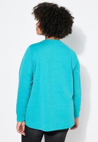 Felpa a maniche lunghe color turchese con design in lettere testurizzate, scollatura a girocollo e polsini a coste. Tessuto morbido con vestibilità rilassata.
