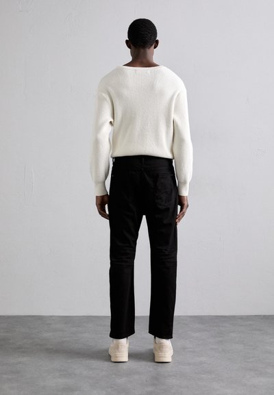 White ribbed sweater, slim black pants, and cream sneakers. The sweater has a wide neckline; pants feature a classic cut.