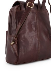 Brun l�æderrygsæk med en struktureret overflade, der har justerbare stropper, en sidelomme og hardwaredetaljer i guldfarve.