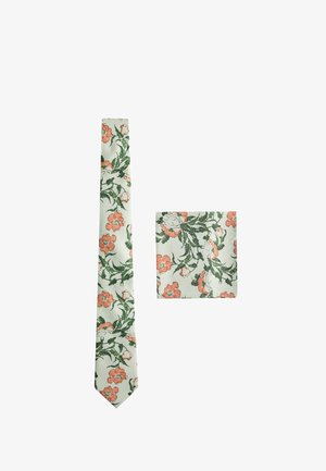 Sæt med slips og lommetørklæde i silke med grønt og orange blomsterprint på hvid baggrund, vist fladt på hvid overflade.