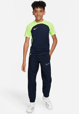 Tenue de sport pour enfants Nike comprenant un haut à manches courtes bleu marine et vert néon, assorti à un pantalon, avec un détail de logo Nike blanc.