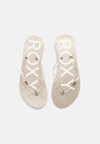 Des tongs beiges avec un motif texturé et une sangle transparente, arborant le logo "ROXY" en blanc sur la semelle et des embellissements sur les sangles.
