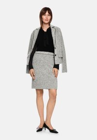 Gray tweed jacket with black accents, layered over a black blouse and gray textured skirt. Black heels complete the outfit.