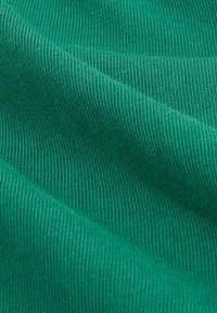 Tela verde texturizada con un patrón acanalado, que muestra un material suave y ligero, con pliegues ondulados que le dan una apariencia suave.