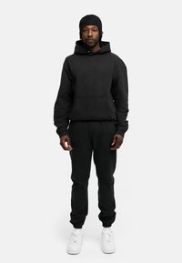 Schwarzer Hoodie und Hose aus weichem Material, mit einer Kängurutasche, Bündchen an den Knöcheln und weißen Turnschuhen, die einen lässigen Look kreieren.