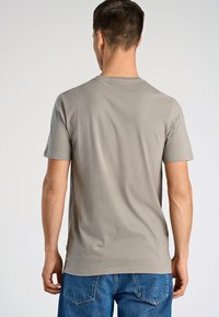 Szara koszulka z krótkim rękawem i okrągłym dekoltem, wykonana z miękkiego materiału, z bezszwowym wykończeniem ramion, połączona z niebieskimi dżinsami z kieszeniami naszytymi.