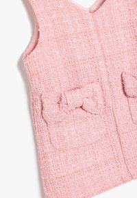 Gilet in tweed rosa con un motivo testurizzato, due tasche a toppa con dettagli a fiocco e design a V. Fodera interna liscia.