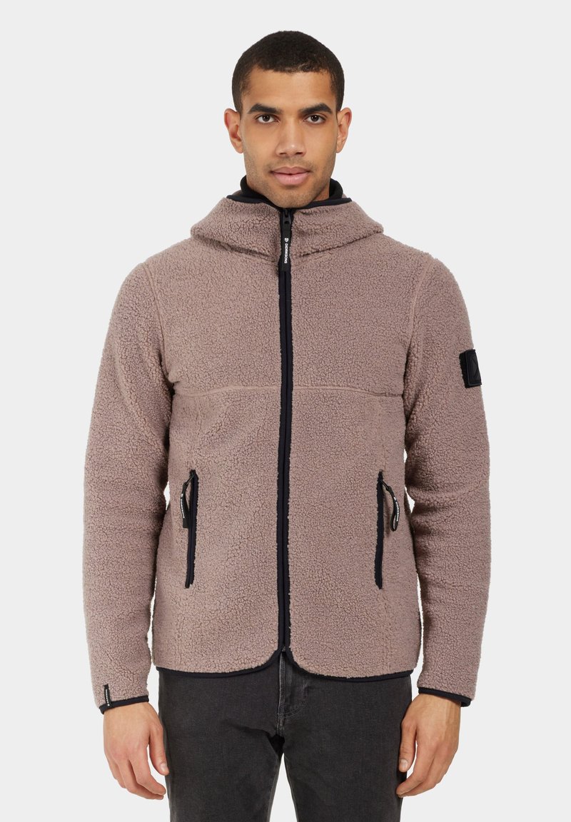 Chaqueta de forro polar en marrón claro con un cuello alto, cremallera frontal y dos bolsillos laterales. Presenta detalles en negro y una superficie texturizada.