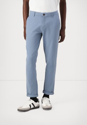 Pantalones de algodón celestes con corte recto, que presentan un cierre de botón marrón, bolsillos laterales y puños doblados. Combinados con zapatillas blancas.