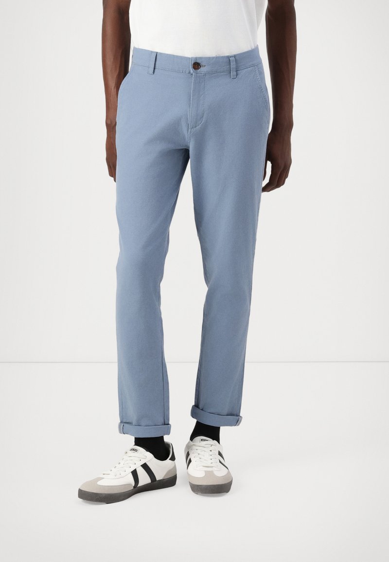 Pantaloni din bumbac de culoare albastru deschis, cu croială dreaptă, având închidere cu nasture maro, buzunare laterale și manșete rulate. Asortați cu adidași albi.