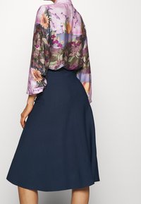 Langärmlige Bluse mit floralem Muster in Pastellfarben und einem Kragen, kombiniert mit einem navyblauen A-Linien-Rock aus einem glatten, strukturierten Stoff.