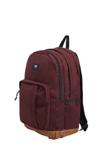 Mochila marrón con un fondo beige, hecha de tela. Presenta múltiples compartimentos con cremalleras y acentos negros. Tiene correas para los hombros acolchadas.