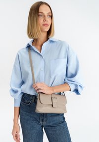 Camicia azzurra chiara con maniche ampie, abbinata a jeans a vita alta e una piccola borsa a tracolla beige con chiusura a patta.