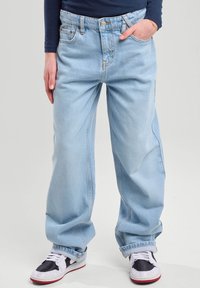 Light blue wide-leg jeans made of denim, featuring a high waist, two front pockets, and visible seams. Paired with black and white sneakers.
