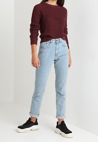 Bordowy sweter z teksturowanej dzianiny zestawiony z jasnoniebieskimi, wysokim stanem jeansami i czarnymi trampkami z białymi podeszwami. Casualowy, dopasowany look.