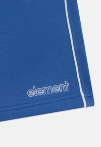 Zila kokvilnas auduma gabals ar baltu akcentu dūrienu, apakšējā malā redzama balta "element" logo. Gluda tekstūra.
