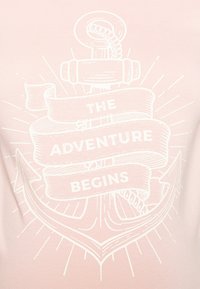 T-shirt rosa com um gráfico branco de uma âncora e fita com o texto "A AVENTURA COMEÇA", enfatizando temas e design náuticos.