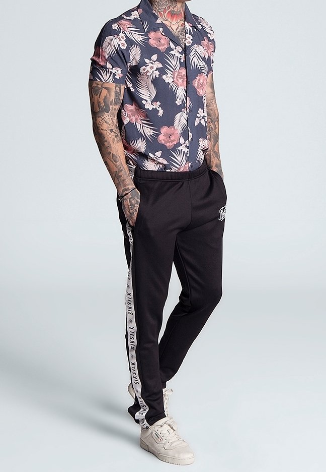Camisa de manga corta azul marino con flores rosas, combinada con pantalones deportivos negros con rayas laterales y texto blanco, usada con zapatillas blancas.