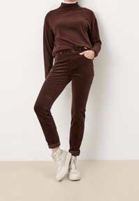 Pantalones de pana marrones con cintura alta, ajuste ceñido y puños enrollados, combinados con un cuello de tortuga marrón a juego y zapatillas ligeras.