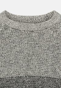 Nahaufnahme von grau- und schwarz gestricktem Stoff mit strukturiertem Rippenkragen auf einem Pullover.