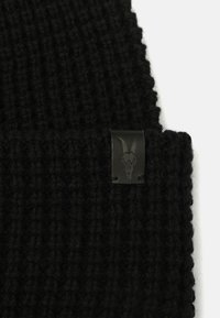 Gorro de punto negro con un patrón de canalé texturizado. Una pequeña etiqueta de cuero con un logo de cráneo de cabra está cosida en el lateral.