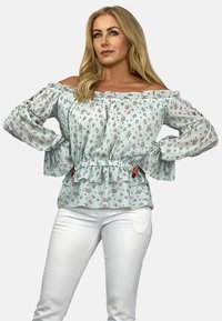 Jasnoniebieska bluzka w kwiaty z dekoltem off-the-shoulder, falbanowym wykończeniem i długimi rękawami. Noszona z białymi spodniami z marszczoną talią.