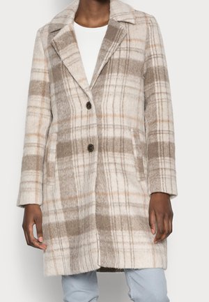 Beżowo-kremowy wełniany płaszcz w kratę o długości do połowy uda, z kołnierzem z klapą i dwoma ciemnymi guzikami, noszony na białej bluzce i jasnoniebieskich dżinsach.