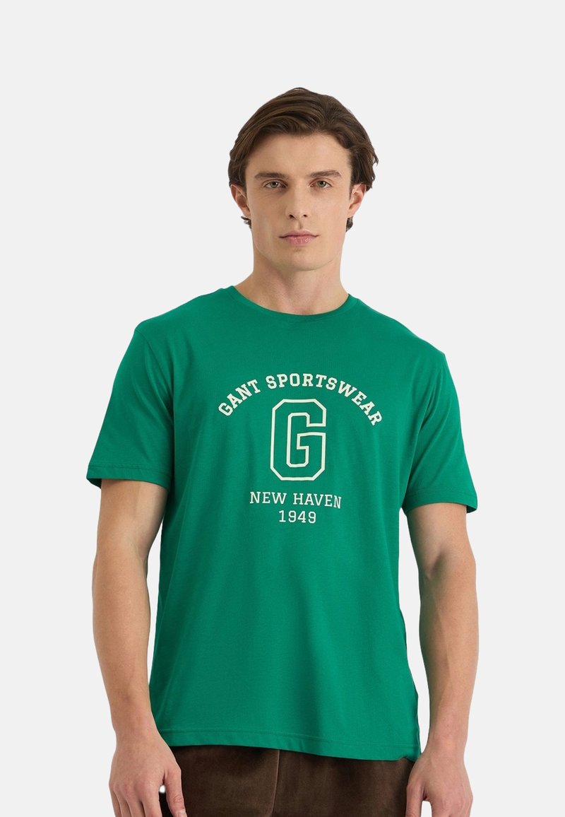 Camiseta de algodón verde de manga corta, con un gráfico blanco que dice "GANT SPORTSWEAR NEW HAVEN 1949" en la parte frontal con una tipografía en negrita.