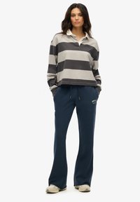 Szara i czarna pasiasta koszulka polo z długim rękawem i kołnierzykiem, zestawiona z granatowymi spodniami dresowymi z logo z przodu. Lekki materiał i luźny krój.