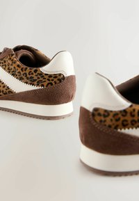 Bruine en witte sneakers met een luipaardprintontwerp, materialen van suède en leer, gestructureerde accenten en een rubberen zool met een zigzagpatroon.