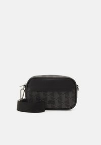 Piccola borsa a tracolla nera con accessori in argento, motivo geometrico, logo "Lacoste" in rilievo e tracolla regolabile su sfondo bianco.