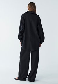 Camicia nera oversize con colletto e maniche lunghe, abbinata a pantaloni neri larghi. Tessuto morbido con un design minimalista.