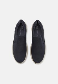 Marineblå slip-on sko laget av semsket skinn med en glatt tekstur, med dekorative sømmer og perforerte detaljer på overdelen. Lett såle.