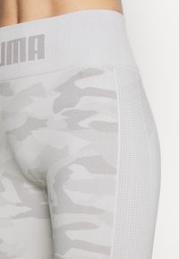 Světle šedé legíny s texturovaným, abstraktním vzorem a síťovinovými detaily. Elastický pas má na vrchu značku "PUMA".